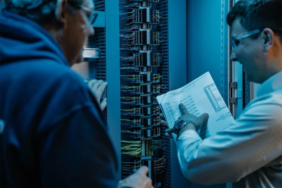 Engineer reviewing documentation beside network equipment racks
